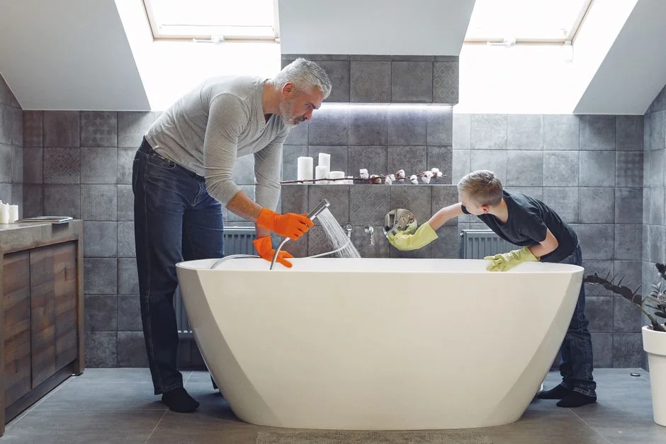 Unidentified person wearing yellow rubber gloves and using a basic sponge to clean a bathroom mirror